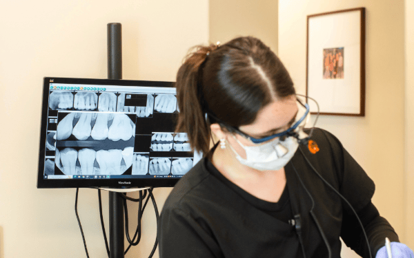 dental assistant working on patient with xrays behind her