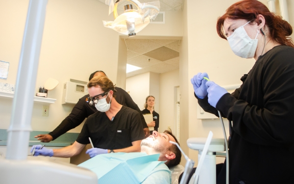 dental patient in chair with dentist and 2 assistants standing by