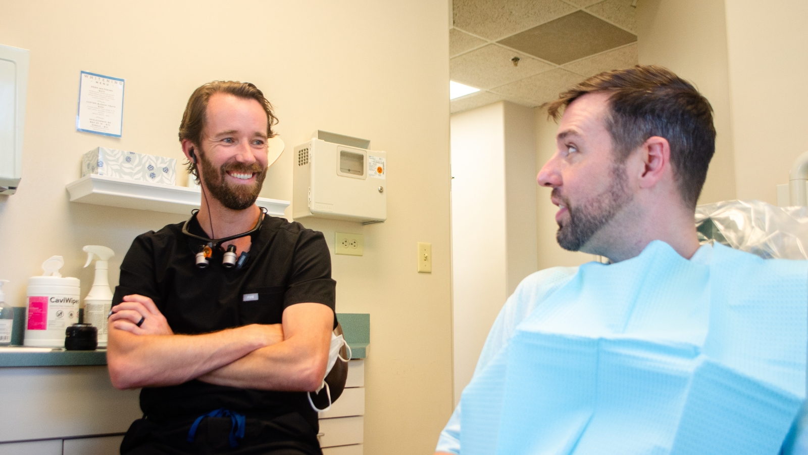 male dentist talking to male patient sitting in dental chair